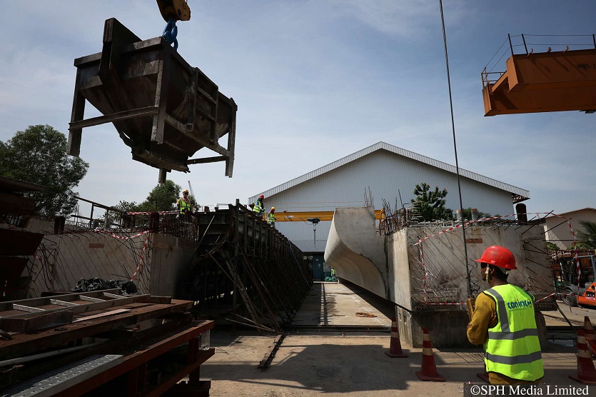 A worker guiding a concrete bucket over a mould as others wait to begin the casting process at the precast yard