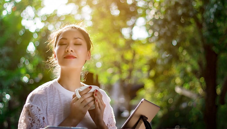 Woman relaxing while holding cup A woman soaking in the sun and greenery